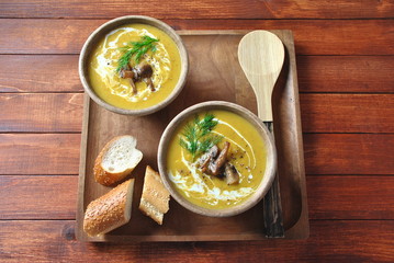 Pumpkin cream soup with cream and mushrooms in two wooden bowls on wooden background