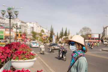 Obraz na płótnie Canvas Caucasian woman wearing sanitary mask outdoors in Da Lat city centre Vietnam. Tourist with medical mask protection against risk of chinese corona virus epidemy in Asia. Anti smog mask pollution.
