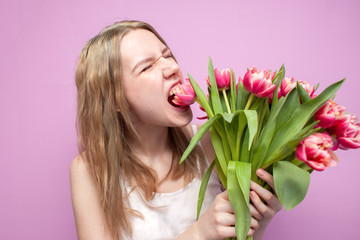 Obraz na płótnie Canvas young beautiful girl holds a bouquet of flowers on a colored pink background, a woman eats tulips