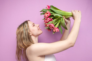 Obraz na płótnie Canvas girl holds and sniffs a bouquet of flowers on a pink background, a beautiful woman with tulips