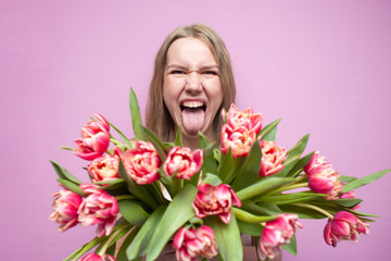 young beautiful girl with a bouquet of flowers on a colored pink background, a woman holds tulips and screams from happiness