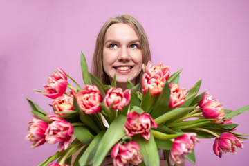 emotional face of a girl in flowers on a pink background, a surprised woman with a bouquet of tulips is smiling