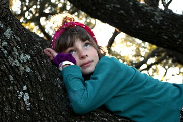 Portrait of a child laying on a branch of an old tree daydreaming