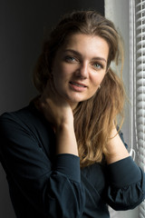 Portrait of a young beautiful girl in a room on a background of a gray wall with shadows, natural light from the window.