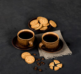 Fototapeta premium Round shortbread cookies in the shape of coins and a Cup of black coffee on a dark gray background in rustic style