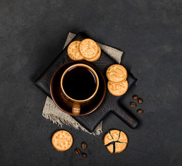 Round shortbread cookies in the shape of coins and a Cup of black coffee on a dark gray background in rustic style