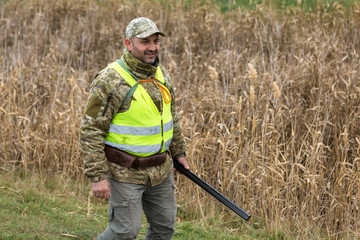 Hunting period, autumn season open. A hunter with a gun in his hands in hunting clothes in the autumn forest in search of a trophy. A man stands with weapons and hunting dogs tracking down the game...