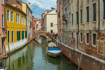 VENICE, ITALY - August 02, 2019: One of the thousands of lovely cozy corners in Venice on a clear sunny day. Locals and tourists strolling along the historical buildings and canals with moored boats