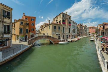 VENICE, ITALY - August 02, 2019: One of the thousands of lovely cozy corners in Venice on a clear sunny day. Locals and tourists strolling along the historical buildings and canals with moored boats