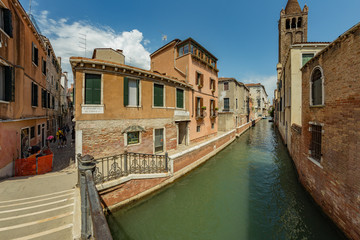 Fototapeta na wymiar VENICE, ITALY - August 02, 2019: One of the thousands of lovely cozy corners in Venice on a clear sunny day. Locals and tourists strolling along the historical buildings and canals with moored boats