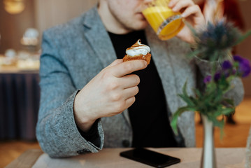 Obraz premium Man drinking fresh orange juice and eating a cupcake in restaurant. Modern smartphone on the table.