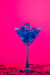Droplets of Drink Spilling Out of The High Glass Goblet with Ice Cubes and Colorful Liquid. Isolated Over Colorful Background.