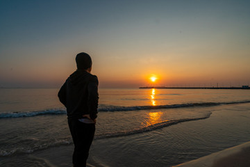 Unknown person watching sunset by the sea at a beach  during golden hour.