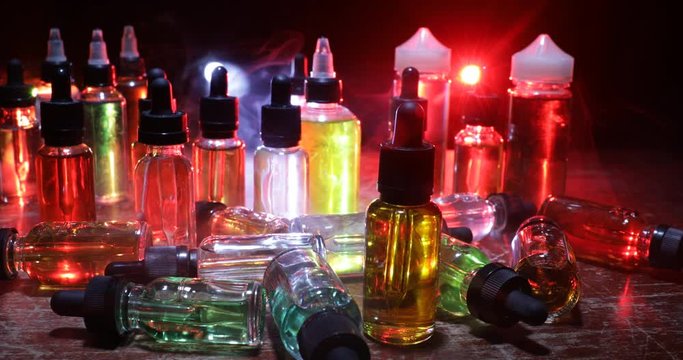Vape concept. Smoke clouds and vape liquid bottles on dark background. Light effects. Useful as background or vape advertisement or vape background. Selective focus