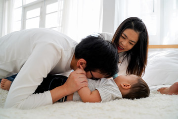 Obraz na płótnie Canvas Family of young Asian father tenderly kissing his baby boy on his stomach with his wife. Man and woman enjoying their time with child