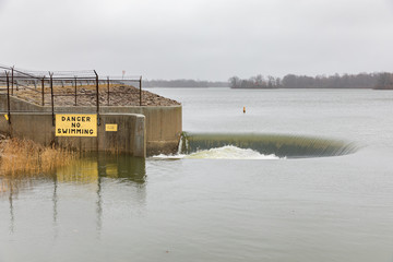 Water flowing over bell-mouth spillway dam after winter storms brought heavy rain and flooding. High water level at Sangchris Lake State Recreation Area