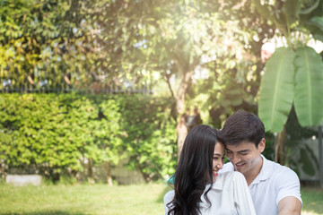 Obraz premium Cute couple have a good time together in front yard,young asian man and woman hug head touch head with happy face and smile with green tree background outdoor with copy space.