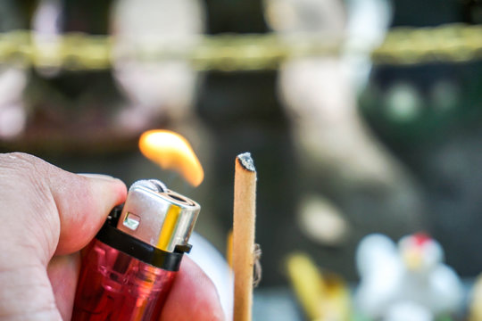 Cropped Image Of Hand Burning Incense Stick With Lighter