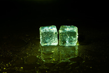 Green ice cubes on black table background.