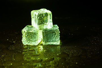 Green ice cubes on black table background.