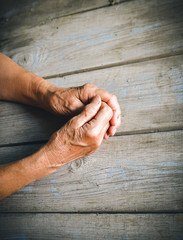 Elderly woman hands, rustic wooden background. Senior with fingers crossed. Wrinkled palms stretched forward. Religion, take care, mothers day concept. Emotions, old people health, love, compassion.