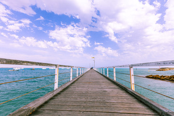Low angle view of long wooden pier in diminishing perspective under beautiful sky