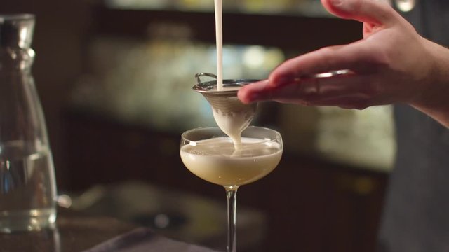 Bartender pours alcohol in glass through a sieve at the bar