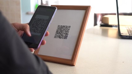 A man scans a QR code from the display. QR code technology: Payment, Transfer, Invoicing, Check-in, Website login, Self-service in the sales area, Participation in promotions