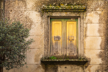 Italy, Sicily, Messina Province, Montalbano Elicona. Moss covered, shuttered window in a stone wall in the medieval hill town of Montalbano Elicona.