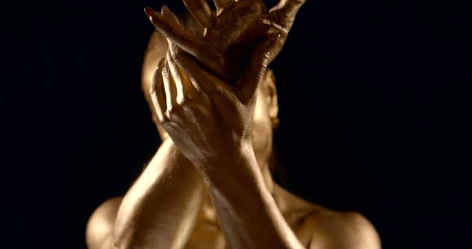 woman is covered golden greasepaint, moving and showing her hands in darkness, detail view
