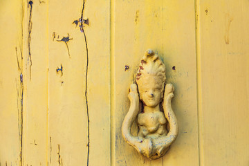 Italy, Sicily, Province of Messina, Novara di Sicilia. Yellow wooden door with a person shaped knocker, in the medieval hill town of Francavilla di Sicilia.