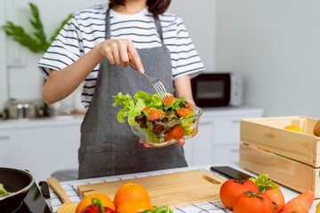 Woman hands holding salad bowl with eating tomato and various green leafy vegetables on the table at the home.