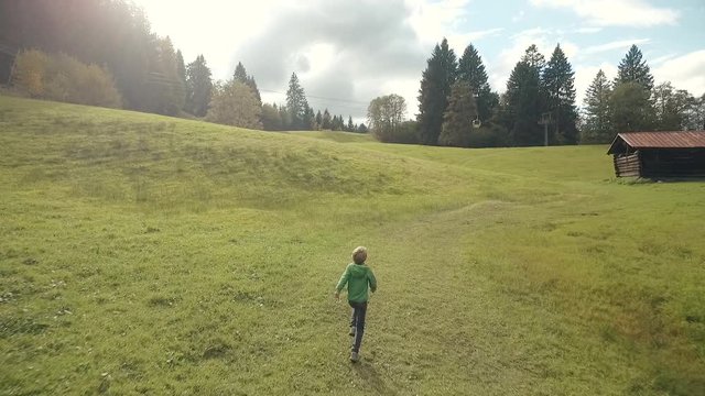 Young boy running over a meadow in the mountains, cable car