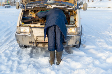 The driver repairs the engine of the car in the winter in the cold.