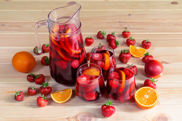 Red wine sangria with fruits in glasses and pitcher on rustic wooden table. Fresh fruits near. Selective focus.