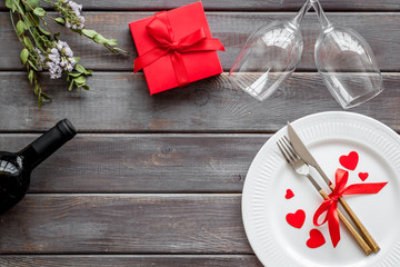 Romantic dinner on Valentines Day. Wine, plate, present box on dark wooden background top-down copy space