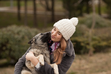 The owner is a beautiful girl in an artificial fur coat holding her Keeshond dog, looking at each other and smiling. Concept: love between dog and owner. Protection of animals.