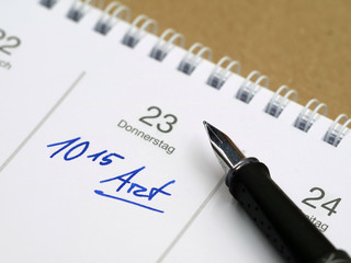 white calendar with german word for doctor's appointment and time written with a fountain pen