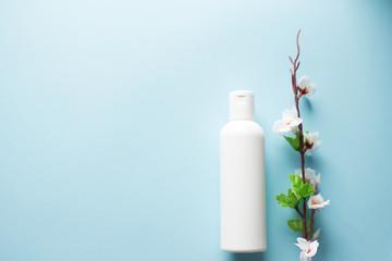 White shower gel bottle and flowering cherry branch on blue background with a copy space.