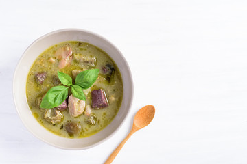 Thai green curry chicken in a bowl and wooden spoon on white table, Thai food