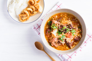 Northern Thai food (Kanom Jeen Nam Ngeaw), rice noodles with spicy soup in a bowl eating with pork rind on white table