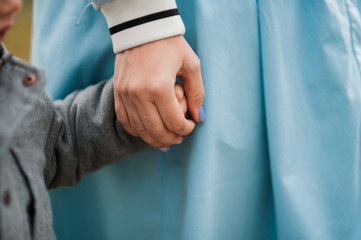 hands of parent and child hold each other tightly against a background of delicate blue clothes of an adult