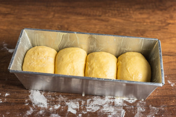 Yellow bread dough in a metal baking tin with flour dusting on wood texture table surface.