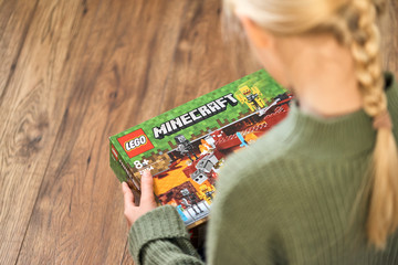 Naklejka premium January 5, 2020, Kaliningrad, Russia. A little girl with blond hair is holding a new box of Lego Minecraft and looks at it.