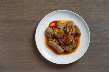 top view of stir fried duck meat with red curry paste in a ceramic dish on wooden table. hot and spicy thai style food menu.