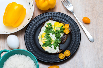 Fried eggs on a black plate with a bowl of basmati rice and fresh tomatoes and peppers