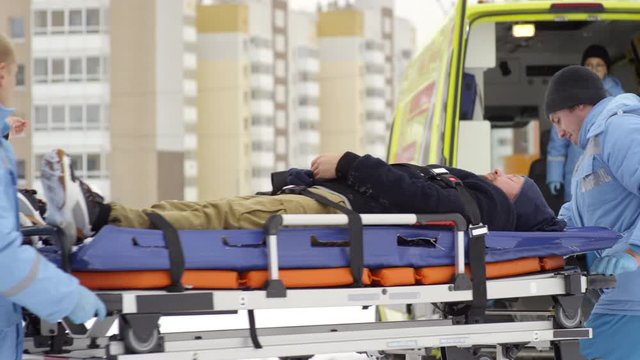 Tracking of paramedics loading stretcher with unconscious man into ambulance on cold winter day