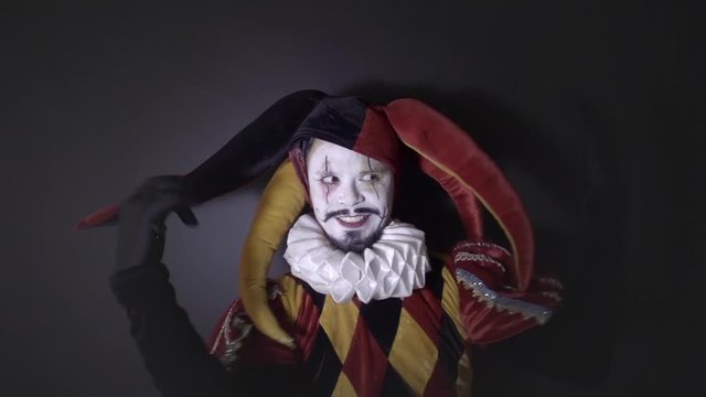Street artist in old costume of Jester, circus performance happy harlequin. Slow motion