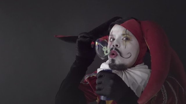 Street artist in costume of Jester making bubbles, circus performance of a happy harlequin. Slow motion