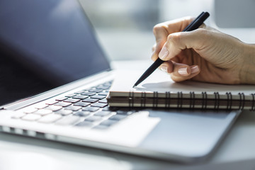 Closeup of girl hand writing in diary on a table with laptop. Focused on a pen